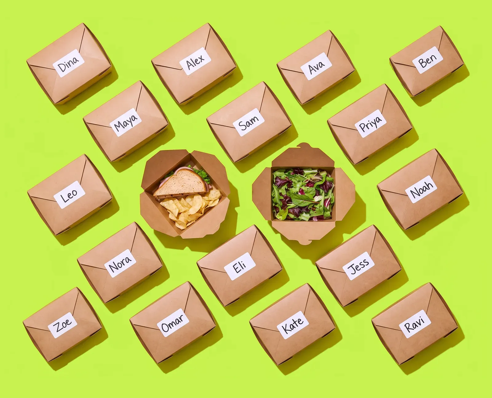 Kraft lunch boxes laid out in rows, each labeled with a first name, two open to show a sandwich with chips and a green salad